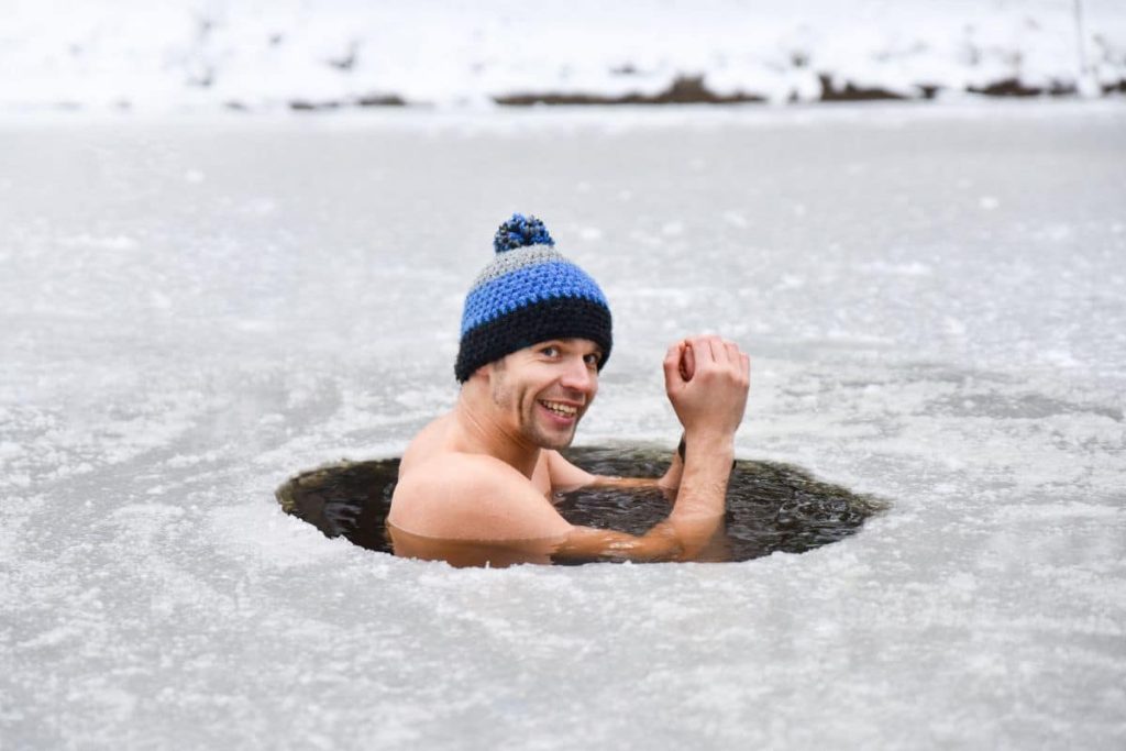 Un homme souriant portant un bonnet nage dans un trou dans la glace.
