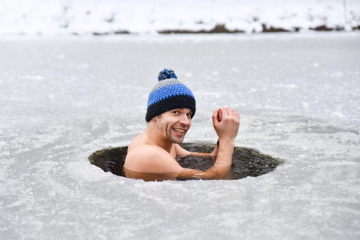 Un homme souriant portant un bonnet nage dans un trou dans la glace.