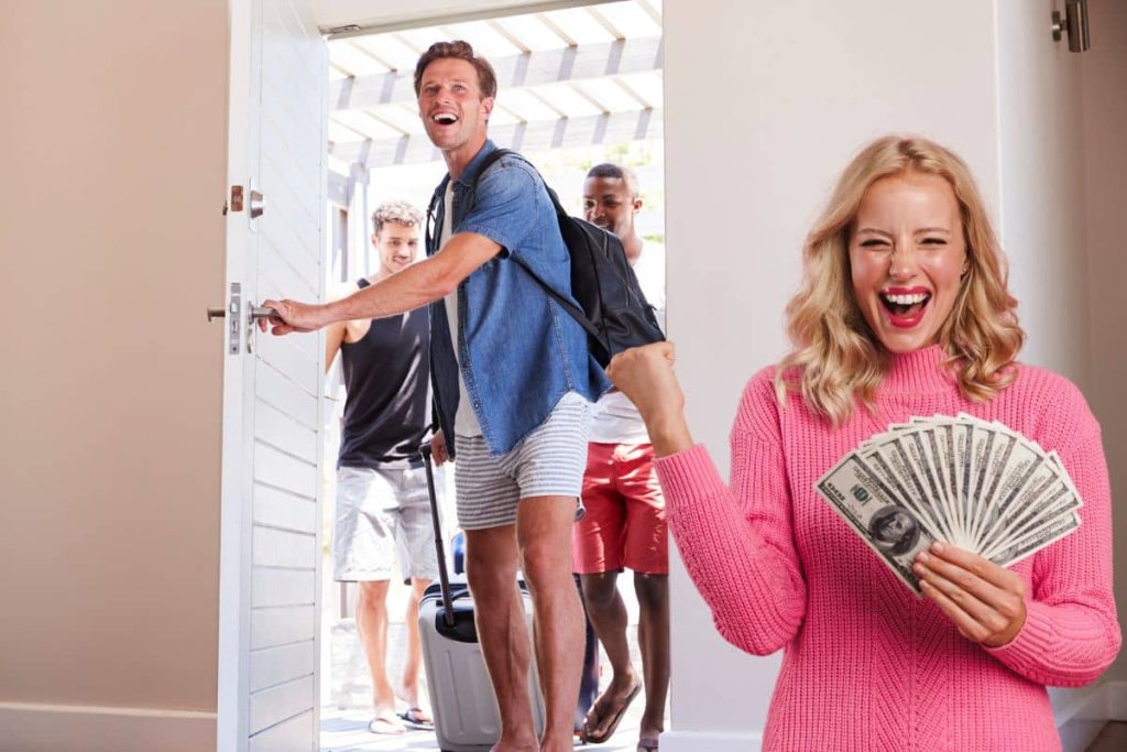 Une femme souriante tenant des billets alors que des vacanciers arrivent avec leurs valises.