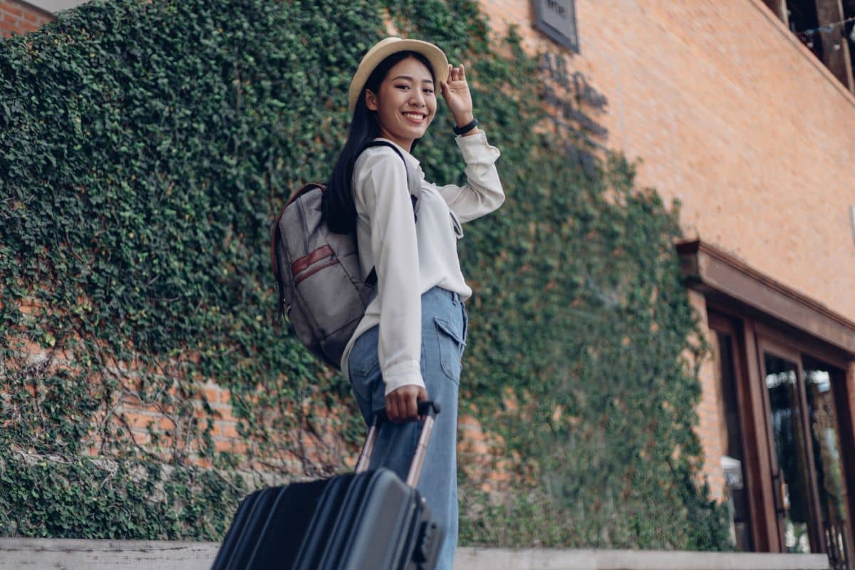 Une femme souriante avec un chapeau et une valise.