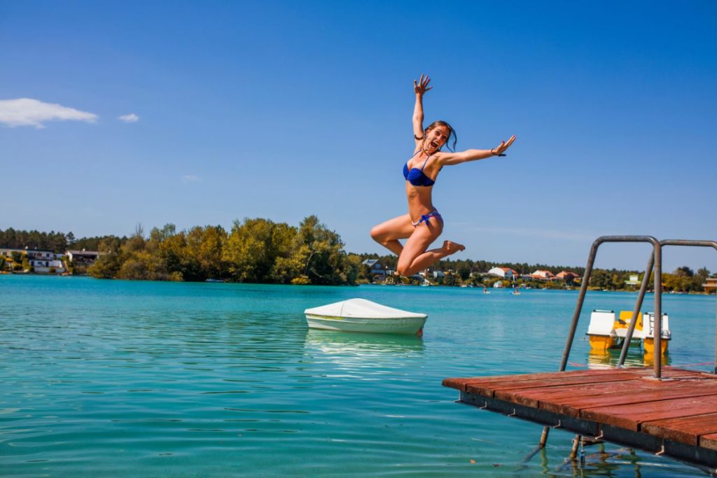 Une femme en maillot de bain bleu saute joyeusement dans un lac.
