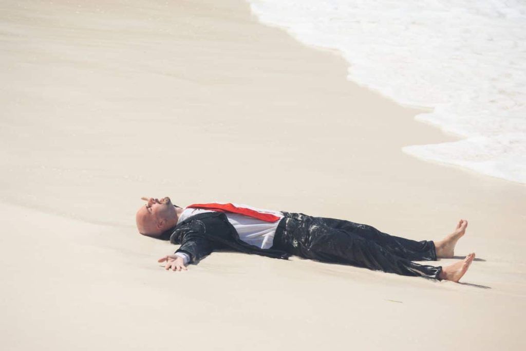 Homme en costume allongé sur une plage.