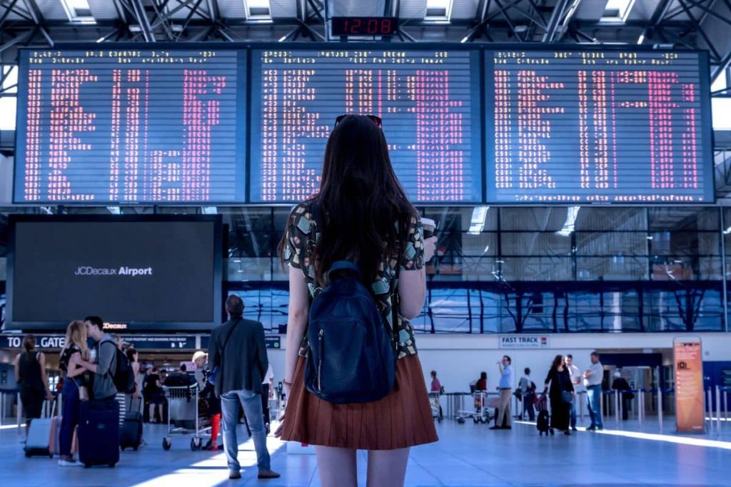 Une femme avec un sac à dos regarde les horaires des vols à l'aéroport.