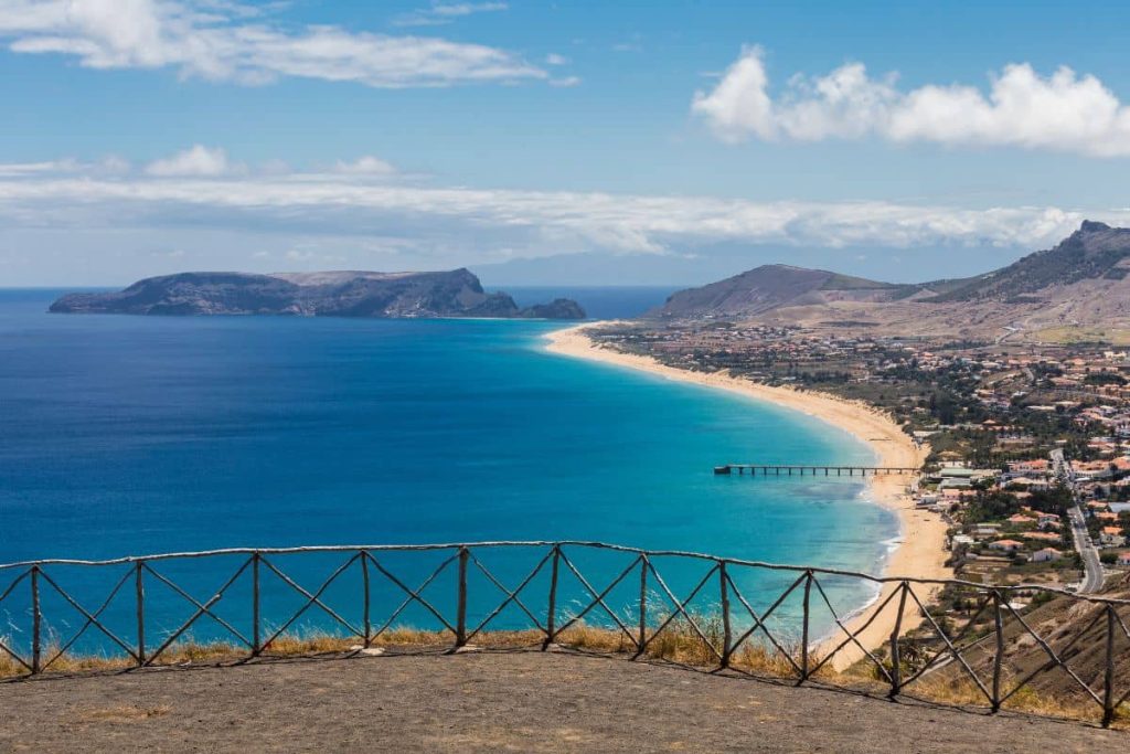 Vue panoramique d'une plage et d'une station balnéaire avec une mer bleue et des montagnes en arrière-plan.