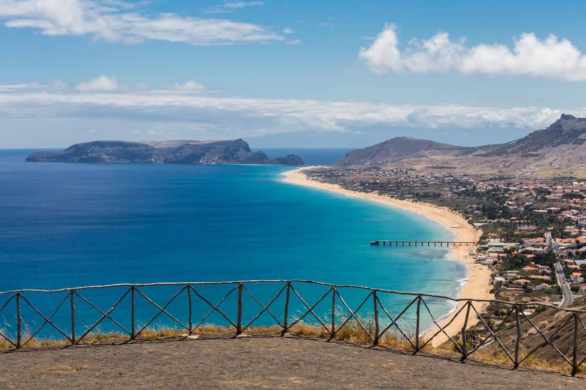 Vue panoramique d'une plage et d'une station balnéaire avec une mer bleue et des montagnes en arrière-plan.