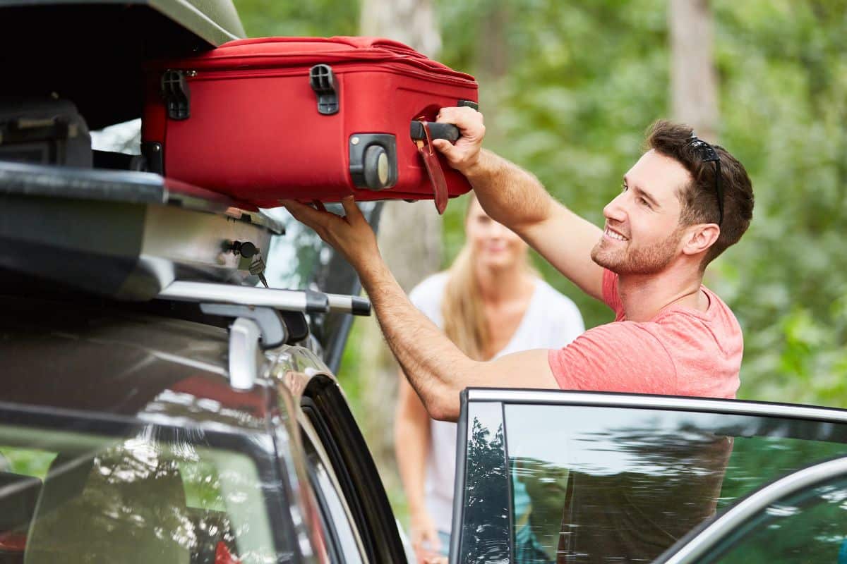 Un homme charge une valise rouge sur le toit d'une voiture